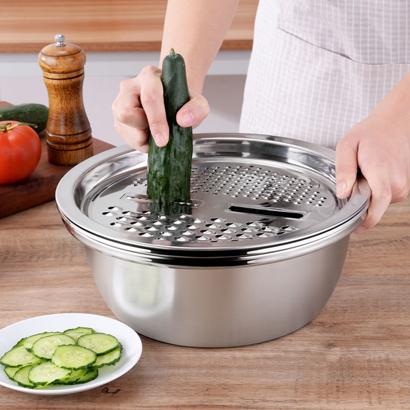 Person using a metal mandoline slicer to cut a cucumber on a wooden countertop.