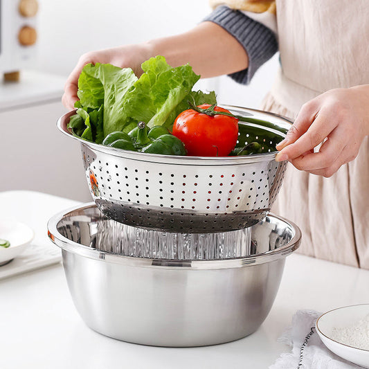 Person transferring vegetables from a colander into a larger metal bowl on a kitchen counter.